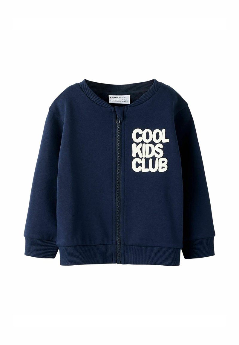 Tumed sinise värviga lastele mõeldud tõmblukuga sviiter, millel on pehme tekstuur ja kreemivärvi tekst "COOL KIDS CLUB". Ribitud varrukad ja helk. 