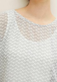 Top bianco trasparente caratterizzato da un motivo a onde nere ripetuto, con scollatura rotonda e una consistenza morbida e liscia.