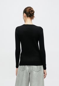 Suéter negro de manga larga con cuello redondo y puños y dobladillo acanalados. Combinado con pantalones gris claro, de corte amplio. Textura sutil.