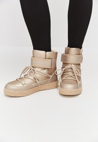 Sneakers beige high-top con suola testurizzata, dotati di chiusura con lacci e strap adesivo, materiale liscio e fodera morbida.