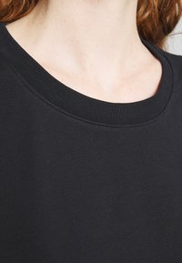 Gros plan sur une personne portant un vêtement noir à col rond, montrant le col, une partie du cou et des cheveux.