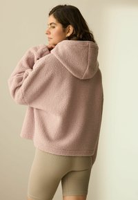Oversized roze fleece hoodie met een gestructureerd oppervlak en capuchon, gecombineerd met beige geribbelde fietsshorts.
