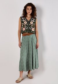 Knitted sleeveless top with floral pattern in white, orange, and green; paired with a green patterned skirt and a brown woven belt.
