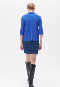 Blå tröja med krage, trekvartsärmar, ihop med en denimkjol. Svarta knähöga stövlar fulländar outfiten.