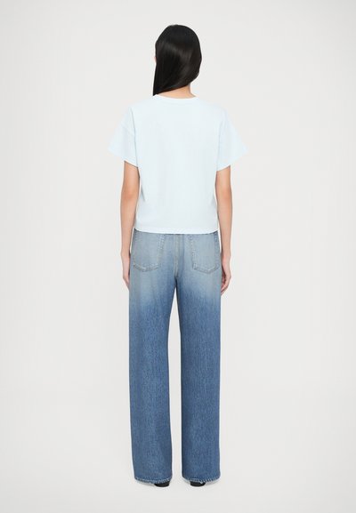 Lys blå cropped t-shirt med korte ærmer, parret med højtaljet, vide bukser med en gradient blå vask og subtil bleget effekt.