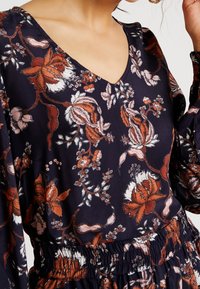 Blumenbluse mit navy Hintergrund. Mit V-Ausschnitt, langen Ärmeln und elastischem Bund. Blumen in den Farben Orange, Weiß und Pink.