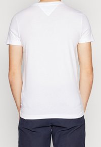 Camiseta blanca de manga corta con escote redondo y un acento triangular en la parte posterior. Fabricada con una tela ligera y suave.