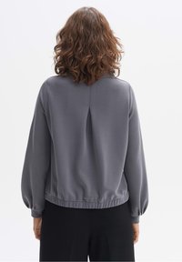Suéter gris con mangas largas, con detalle de pliegue en la parte trasera y dobladillo fruncido. Tela suave con un ajuste relajado.