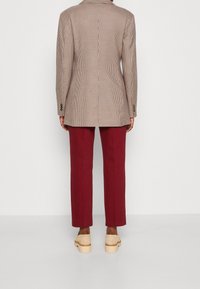 Blazer marrón a cuadros con un ajuste entallado, combinado con pantalones burdeos y zapatos de plataforma beige. Textura suave y diseño estructurado.