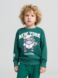 Felpa verde con una scimmia cartoon con occhiali da sole e una mazza. Testo "NEW YORK HIGH SCHOOL" stampato in modo evidente. Materiale morbido di cotone.