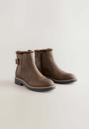 Pruunid pahkluusaapad kunstkarvaviimistlusega, külgsiibri ja reguleeritava rihmaga. Sile naha pealis ja madal jäme konts.