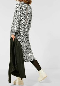Abito midi a motivi in bianco e nero con maniche lunghe; presenta una zip sul retro ed è abbinato a una giacca di pelle nera e stivaletti chiari.