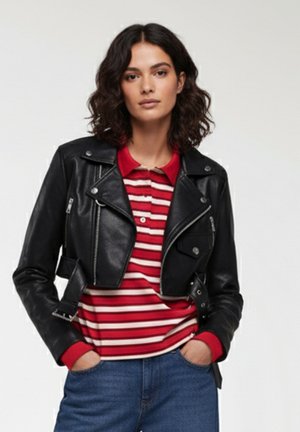 Giacca in pelle nera cropped da biker con accessori in argento, abbinata a una maglietta polo a righe rosse e bianche e jeans in denim blu.