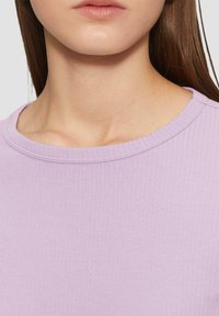 Lichtpaarse geribde trui met een ronde hals. De stof is glad en heeft een subtiele glans, met nette stiksels langs de kraag.