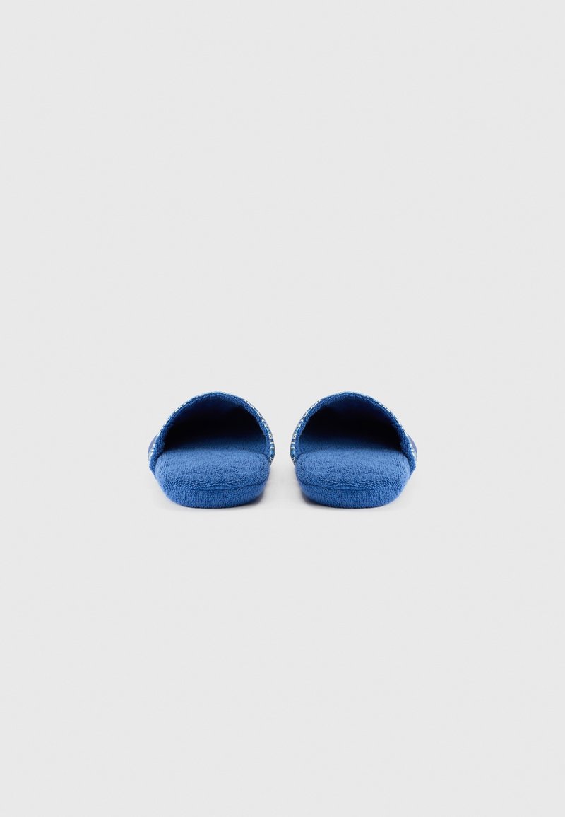 Blaue Hausschuhe aus Stoff mit offenem Zehendesign, weicher strukturierter Oberfläche und gemustertem Besatz. Flache Sohle für den Gebrauch im Innenbereich.