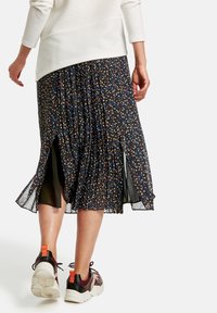 Kvinde iført en sort plisseret midi-nederdel med små blomsterprint, parret med en hvid top og sorte, røde sneakers, der går væk.