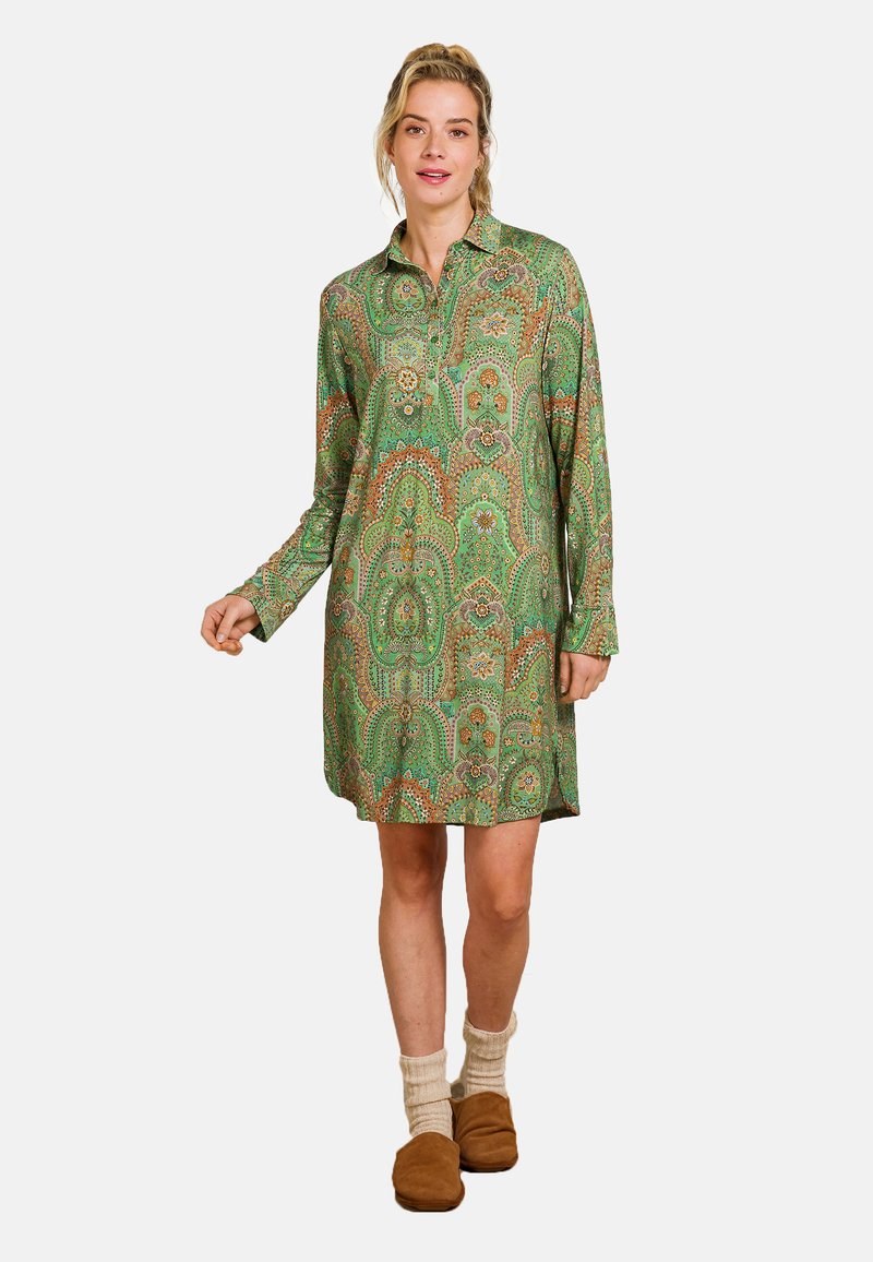 Green paisley-patterned shirt dress with long sleeves, collar, and button placket; wool socks and brown slippers complete the look.