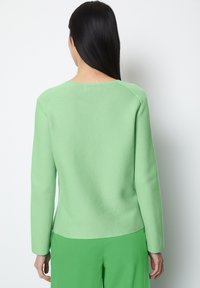 Green knitted sweater with a crew neckline and long sleeves, featuring a smooth texture and a relaxed fit at the waist.