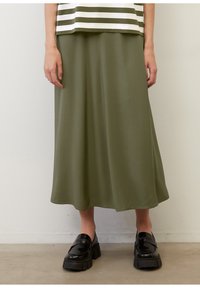 Jupe de mi-longueur vert olive en tissu lisse, avec une silhouette en A. Associée à des mocassins noir épais pour le contraste.
