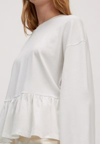 Witte top met lange mouwen en een relaxte pasvorm, voorzien van een gerimpelde zoom en zachte, lichtgewicht stof. Eenvoudig ontwerp zonder zichtbare patronen of accenten.