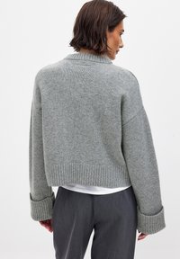 Afskåret grå trøje lavet af blødt strikstof, med ribbet kant og oversize manchetter. Enkel design med minimale detaljer.
