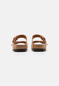 Bruine leren sandalen met twee verstelbare banden, kurken voetbed, gestructureerde zool en een bloemenaccent op een band. Achteraanzicht getoond.
