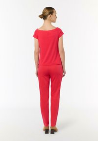 Czerwony dwuczęściowy zestaw składający się z góry z krótkim rękawem i dopasowanych spodni. Góra ma okrągły dekolt, a obie części mają gładką fakturę.