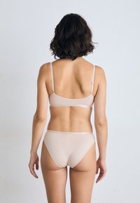 Light beige wireless bra and high-waisted brief set. Soft fabric with smooth texture. Adjustable straps and minimalistic design.