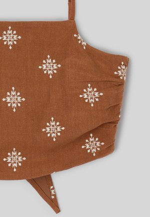 Masque facial en tissu marron avec motifs géométriques d’étoiles blanches et boucles d’oreilles ajustables sur fond gris.