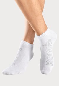 White ankle socks made of soft material, featuring a subtle "Bench." logo in grey, ribbed cuffs, and a seamless toe design.