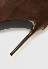 Καφέ καστόρινο γυναικείο παπούτσι με ψηλό τακούνι στιλέτο, λεπτό και γυαλιστερό μαύρο. Ομαλή υφή με στρογγυλή μύτη και σχεδιασμό με στενό μπροστινό μέρος.