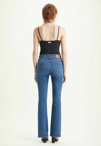 Vaqueros acampanados de mezclilla azul con cintura alta, con bolsillos traseros y una etiqueta de cuero. Combinados con una camiseta negra sin mangas.