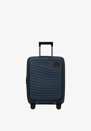 Valise cabine rigide bleu marine avec texture rayée, quatre roues, poignée télescopique et poche zippée sur le compartiment avant.