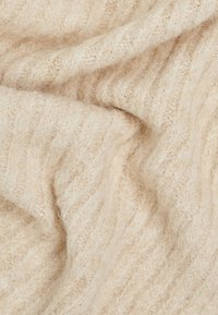 Tessuto lavorato a maglia color crema con una finitura morbida e testurizzata, caratterizzato da un sottile motivo a coste, che mostra pieghe e drappeggi.