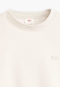 Felpa beige chiaro con collo a girocollo a coste, caratterizzata da un piccolo logo Levi's ricamato sul davanti. Tessuto morbido e testurizzato.
