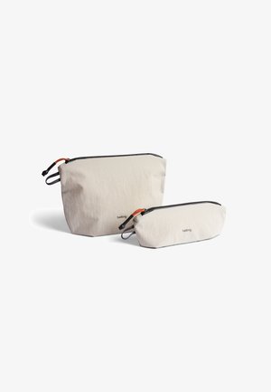 Trousse de toilette en tissu beige clair, une grande et une petite, avec des fermetures éclair noires et des accents orange. Présente une texture subtile et un logo.
