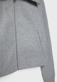 Gray wool blend zippered jacket with a smooth texture, ribbed sleeves, and a concealed side pocket. Simple, functional design.