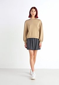 Beige Langarm-Sweatshirt, kombiniert mit einem dunkel gestreiften Rock, getragen mit weißen Sneakers. Das Outfit zeichnet sich durch lockere Passformen und weiche Materialien aus.