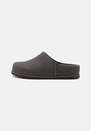 Tmavosivý nazúvací klump s uzavretou špičkou, nízkym opätkom a logom UGG na boku, zobrazený na jednoduchom bielom pozadí.