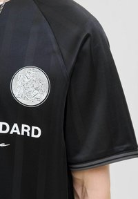 Mustmustelane spordijerseys, millel on tekstuuriga viimistlus, ringikujuline hõbedane emblem ja valge tekst. Kujundusele on lisatud peeneid vertikaalseid jooni ja halli aktsenti.
