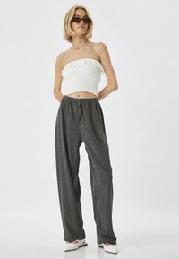 Witte, gerimpelde strapless top gecombineerd met donkere, wijde pantalon. De pantalon heeft een subtiele gestreepte textuur en een elastische tailleband.