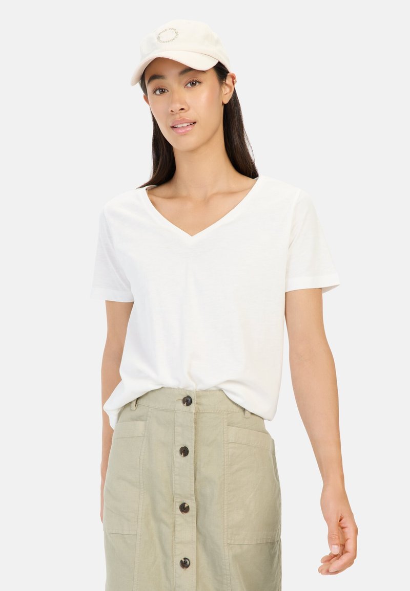 Hvid, kortærmet V-hals t-shirt kombineret med en højtaljeret, grøn knap-op nederdel. Kappen er beige med et cirkulært logo.