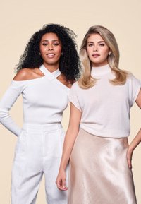 Deux mannequins se tiennent côte à côte. L'un porte un haut blanc à épaule dénudée en côte avec des manches longues et un pantalon blanc taille haute. L'autre porte un haut rose clair à manches courtes et une jupe midi lisse et brillante.