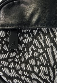 Tecido estruturado a preto e branco com uma estampa texturizada de animal, detalhes em pele preta e um detalhe em metal com o logótipo Jordan em preto.