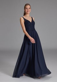 Abito da sera blu navy con corpetto aderente caratterizzato da un ricco lavoro di perline e una gonna in chiffon a strati fluente, completato da spalline sottili.