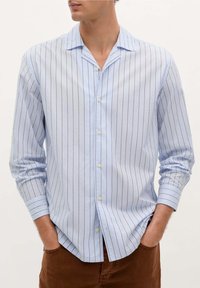 Camisa abotonada de color azul claro con rayas verticales en azul oscuro y blanco, con un cuello casual y mangas largas.