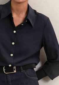 Navy blue long-sleeve shirt with a classic collar, featuring decorative silver buttons and smooth fabric, paired with a black belt and denim.