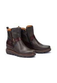 Botas de tobillo de cuero marrón con cremallera lateral, correa decorativa con hebilla y suela de goma texturizada para un buen agarre.