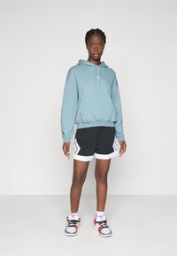 Ljusblå huvtröja med känguruficka, kombinerad med svarta shorts med vita accenter och geometriska mönster. Bärs med flerfärgade sneakers.