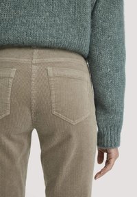 Beige corduroy broek met verticale ribbels en twee achterzakken, gecombineerd met een turquoise gebreide trui met een ribbelmanchet.